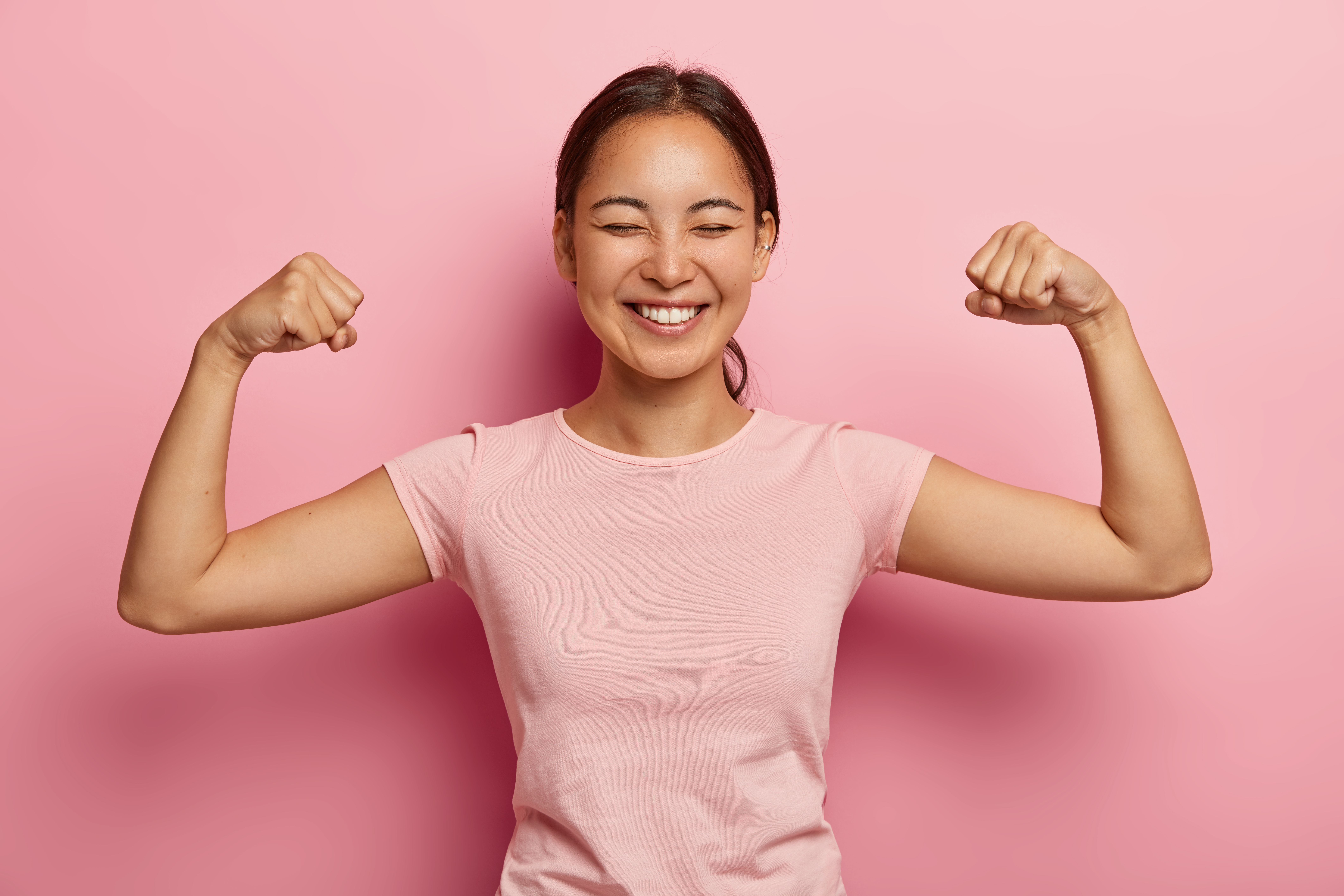 1630052998-strong-powerful-asian-woman-with-dark-combed-hair-toothy-smile-raises-arms-shows-biceps-has-piercing-ear-wears-casual-rosy-t-shirt-models-against-pink-wall-look-my-muscles.jpg